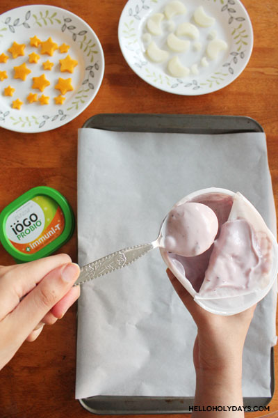 A hand dollops yogurt on a lined baking sheet to make yogurt bark.